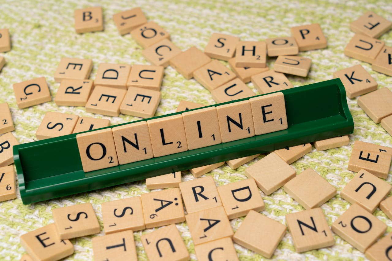 Which English Proficiency Exam Is Actually Easier? Scrabble tiles spelling 'online' on a green tray amidst scattered tiles, symbolizing digital connectivity and language.