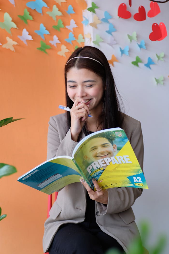 Smiling young woman reading a colorful educational book in a creatively decorated indoor space.