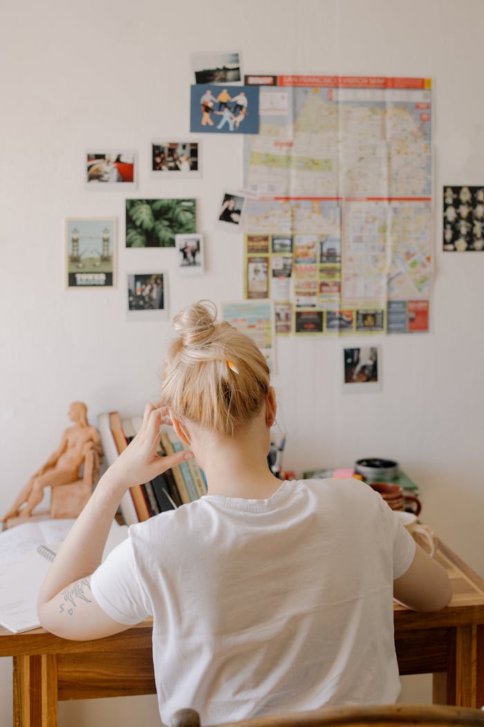 Title: IELTS vs PTE vs OET — Which Exam Should You Take? A student sitting at a desk studying, surrounded by books and wall posters, emphasizing concentration and learning.