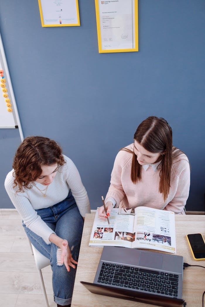 Two women discussing plans in an office using a laptop and magazine